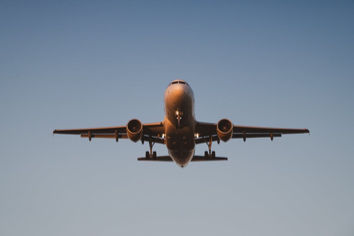 A commercial airplane descends against a clear blue sky, illuminated by dawn light.