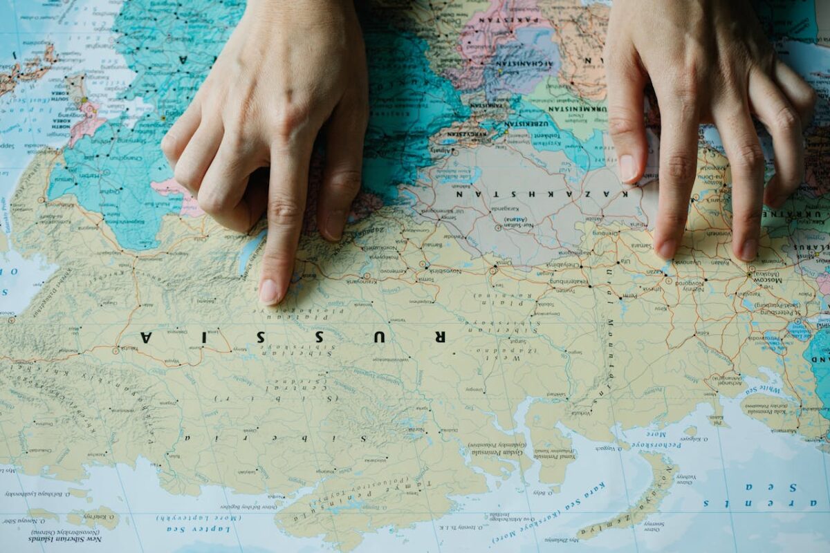 Close-up of hands pointing at Russia on a detailed world map.